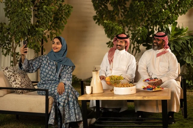 التقاط صورة سيلفي عبر الهاتف المحمول، ضيافة وحلوى العيد، حسن استقبال وإكرام الضيف، فرحة وبهجة الابناء في ايام العيد السعيد, التجمعات والزيارات الاسرية في الأعياد والمناسبات الاسلامية, رجل عربي خليجي سعودي يرتدي الثوب التقليدي يجلس مع أحفاده بإيماءات الفرح والسرور