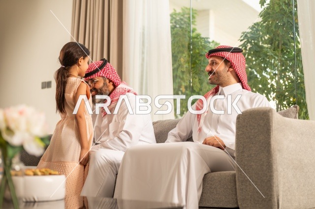 ضيافة وحلوى العيد، حسن استقبال وإكرام الضيف، صلة الرحم والترابط الاسري, فرحة وبهجة الابناء في ايام العيد السعيد, التجمعات والزيارات الاسرية في الأعياد والمناسبات الاسلامية, رجل عربي خليجي سعودي يرتدي الثوب التقليدي يجلس مع أحفاده بإيماءات الفرح والسرور