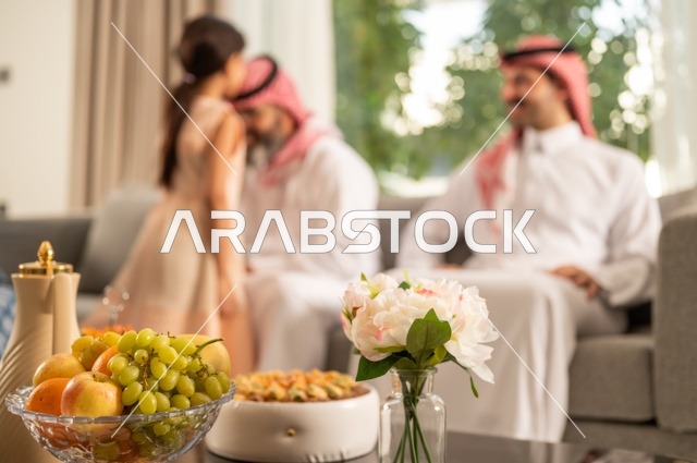 ضيافة وحلوى العيد، حسن استقبال وإكرام الضيف، صلة الرحم والترابط الاسري, فرحة وبهجة الابناء في ايام العيد السعيد, التجمعات والزيارات الاسرية في الأعياد والمناسبات الاسلامية, رجل عربي خليجي سعودي يرتدي الثوب التقليدي يجلس مع أحفاده بإيماءات الفرح والسرور