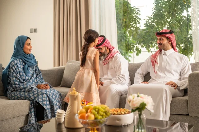ضيافة وحلوى العيد، حسن استقبال وإكرام الضيف، صلة الرحم والترابط الاسري, فرحة وبهجة الابناء في ايام العيد السعيد, التجمعات والزيارات الاسرية في الأعياد والمناسبات الاسلامية, رجل عربي خليجي سعودي يرتدي الثوب التقليدي يجلس مع أحفاده بإيماءات الفرح والسرور