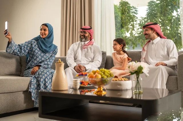 التقاط صورة سيلفي عبر الهاتف المحمول، ضيافة وحلوى العيد، حسن استقبال وإكرام الضيف، فرحة وبهجة الابناء في ايام العيد السعيد, التجمعات والزيارات الاسرية في الأعياد والمناسبات الاسلامية, رجل عربي خليجي سعودي يرتدي الثوب التقليدي يجلس مع أحفاده بإيماءات الفرح والسرور
