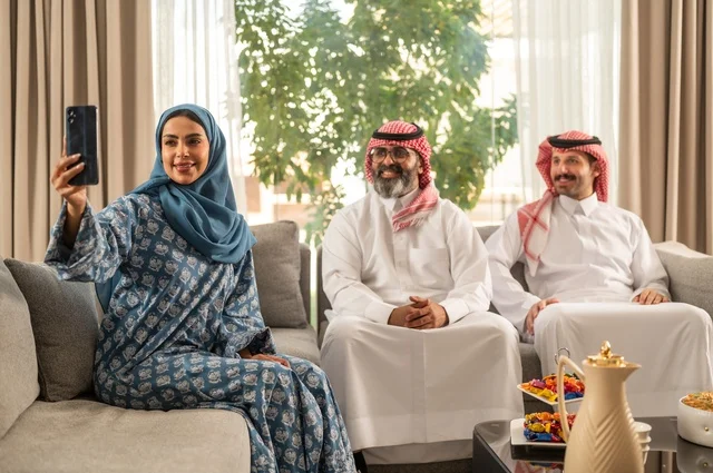 التقاط صورة سيلفي عبر الهاتف المحمول، ضيافة وحلوى العيد، حسن استقبال وإكرام الضيف، فرحة وبهجة الابناء في ايام العيد السعيد, التجمعات والزيارات الاسرية في الأعياد والمناسبات الاسلامية, رجل عربي خليجي سعودي يرتدي الثوب التقليدي يجلس مع أحفاده بإيماءات الفرح والسرور