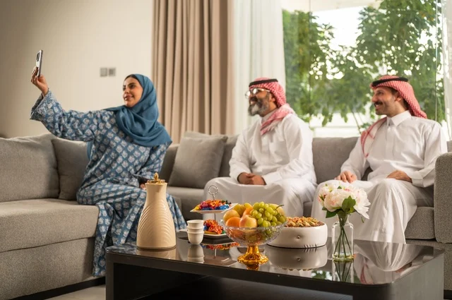 التقاط صورة سيلفي عبر الهاتف المحمول، ضيافة وحلوى العيد، حسن استقبال وإكرام الضيف، فرحة وبهجة الابناء في ايام العيد السعيد, التجمعات والزيارات الاسرية في الأعياد والمناسبات الاسلامية, رجل عربي خليجي سعودي يرتدي الثوب التقليدي يجلس مع أحفاده بإيماءات الفرح والسرور