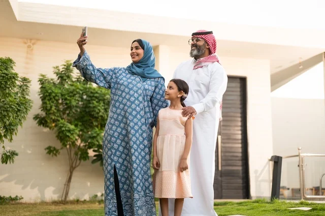 Taking a souvenir selfie with your mobile phone, a chalet and a recreational resort in the Kingdom, enjoying the summer vacation with the family, gestures of happiness and pleasure, having a fun and refreshing time in the summer, a family atmosphere full of love, a smiling Saudi Arabian Gulf family walking in the park