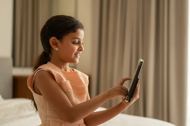 The concept of e-learning, following lessons remotely via the Internet, educational scientific curricula, a Saudi Arabian Gulf girl wearing a dress sitting on the bed holding a tablet in her hand, using a modern and advanced technical device