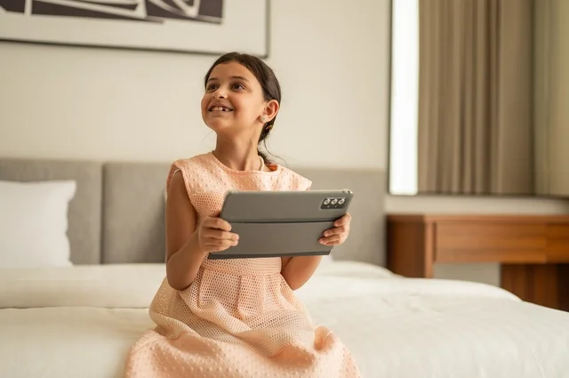 The concept of e-learning, following lessons remotely via the Internet, educational scientific curricula, a Saudi Arabian Gulf girl wearing a dress sitting on the bed holding a tablet in her hand, using a modern and advanced technical device