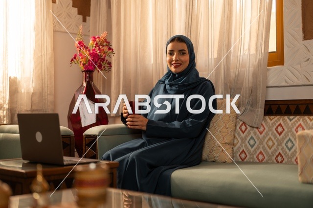 Spending time sipping a favorite drink, vitality and energy from drinking caffeine, enjoying hot beverages and warm winter herbs, a young Arab Gulf Saudi woman wearing an abaya and hijab holding a cup of coffee and enjoying moments of calm and relaxation.