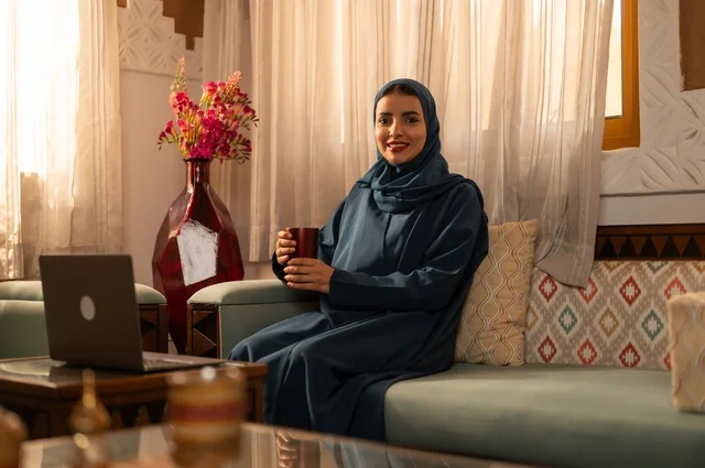 قضاء الوقت باحتساء المشروب المفضل, الحيوية والنشاط عن شرب الكافئيين, الاستمتاع بالمشروبات الساخنة والأعشاب الشتوية الدافئة, شابة عربية خليجية سعودية ترتدي العباءة والحجاب تمسك كوب من القهوة و تستمتع بلحظات الهدوء والراحة