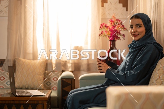 Spending time sipping a favorite drink, vitality and energy from drinking caffeine, enjoying hot beverages and warm winter herbs, a young Arab Gulf Saudi woman wearing an abaya and hijab holding a cup of coffee and enjoying moments of calm and relaxation.