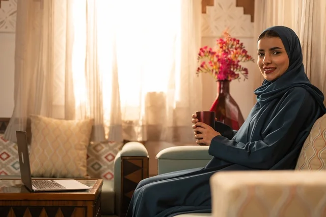 Spending time sipping a favorite drink, vitality and energy from drinking caffeine, enjoying hot beverages and warm winter herbs, a young Arab Gulf Saudi woman wearing an abaya and hijab holding a cup of coffee and enjoying moments of calm and relaxation.