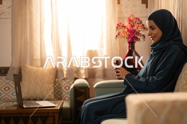 قضاء الوقت باحتساء المشروب المفضل, الحيوية والنشاط عن شرب الكافئيين, الاستمتاع بالمشروبات الساخنة والأعشاب الشتوية الدافئة, شابة عربية خليجية سعودية ترتدي العباءة والحجاب تمسك كوب من القهوة و تستمتع بلحظات الهدوء والراحة