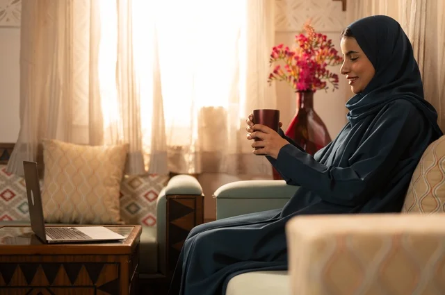 Spending time sipping a favorite drink, vitality and energy from drinking caffeine, enjoying hot beverages and warm winter herbs, a young Arab Gulf Saudi woman wearing an abaya and hijab holding a cup of coffee and enjoying moments of calm and relaxation.