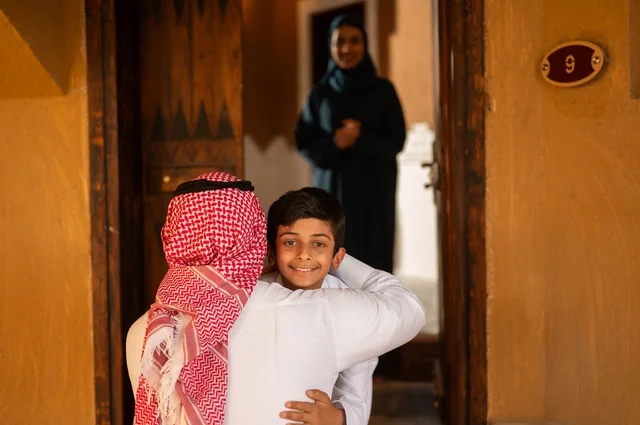 The reception and embrace at the door express love and longing, the familiarity and affection between parents and children, happy family atmospheres filled with warmth and tenderness. An Arab Gulf Saudi family wearing traditional Saudi attire during a family gathering, the warm family reunion and family bonding.