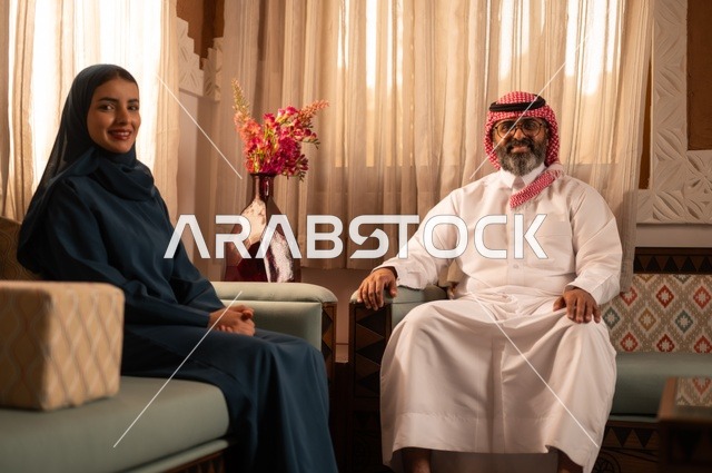 امتلاك بيت جديد، زوجين عربيين خليجيين سعوديين يرتديان الزي السعودي يجلسان على الاريكة ويقومان بتبادل الأحاديث، مفهوم الراحة والاسترخاء، حوارات ونقاشات بين الزوجين، الاستقرار العائلي في المنزل الجديد، الألفة والمحبة بين الأزواج