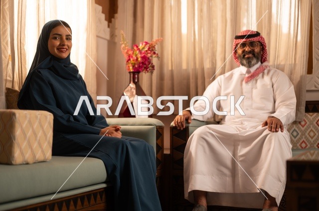 امتلاك بيت جديد، زوجين عربيين خليجيين سعوديين يرتديان الزي السعودي يجلسان على الاريكة ويقومان بتبادل الأحاديث، مفهوم الراحة والاسترخاء، حوارات ونقاشات بين الزوجين، الاستقرار العائلي في المنزل الجديد، الألفة والمحبة بين الأزواج