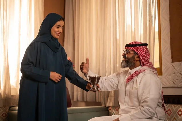 استخدام خشب العود في المناسبات الاجتماعية و الدينية ، التطيب والتعطر  للاستعداد للخروج ، امرأة ترتدي عباءة تحمل حامل البخور( المبخرة )  تقوم بتبخير زوجها، رجل عربي خليجي سعودي يرتدي الزي السعودي يجلس على الاريكة، مفهوم الراحة والاسترخاء، الألفة والمحبة بين الأزواج