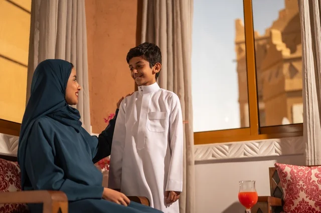 Raising children and caring for them, strengthening the bonds of love and family cohesion, enjoying spending time with children, a Gulf Arab Saudi mother in a hijab sitting with her son in the living room, the concept of affection and tenderness among mothers, gestures of happiness and joy.