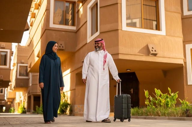 قضاء رحلة صيفية مسلية، مفهوم السياحة في إجازة الصيف، زوجان عربيان خليجيان سعوديان يجران حقائب الامتعة، تعابير وايماءات السعادة والسرور، عائلة تقضي وقت ممتع، الاستعداد للسفر في جولة سياحية