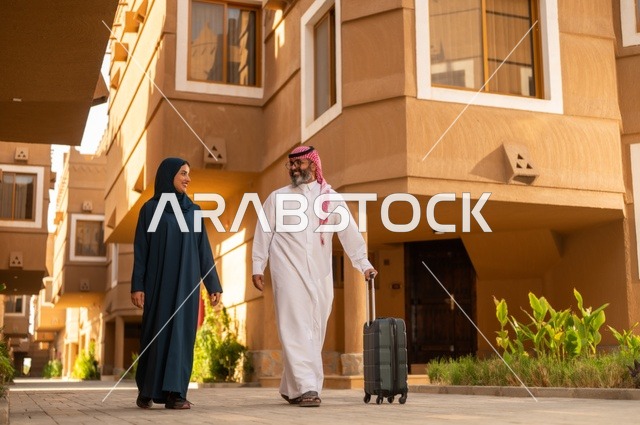 قضاء رحلة صيفية مسلية، مفهوم السياحة في إجازة الصيف، زوجان عربيان خليجيان سعوديان يجران حقائب الامتعة، تعابير وايماءات السعادة والسرور، عائلة تقضي وقت ممتع، الاستعداد للسفر في جولة سياحية