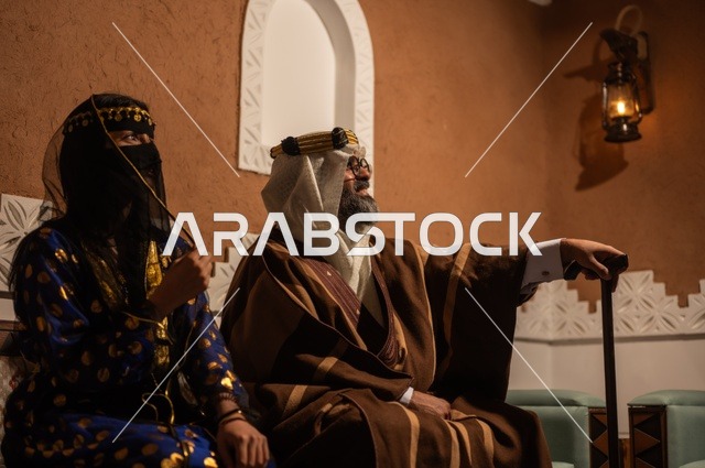 Gestures of pride and honor in the Saudi identity, the anniversary of the establishment of the first Saudi state in 1727 AD, an Arab Gulf couple wearing traditional attire during holidays and national occasions sitting in one of the heritage houses in the old style, the concept of love for the homeland and belonging to it.