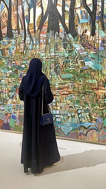 A traditional Saudi outfit, reviving the Gulf folk heritage, a picture from behind of an Arab Gulf Saudi woman wearing a black abaya and hijab standing in front of the Al-Bujairi Historical Museum in Riyadh, on Saudi Foundation Day, a UNESCO World Heritage site, the civilization and history of the Kingdom of Saudi Arabia, the mud houses in Al-Dar'iya Al-Bujairi in the city of Riyadh.