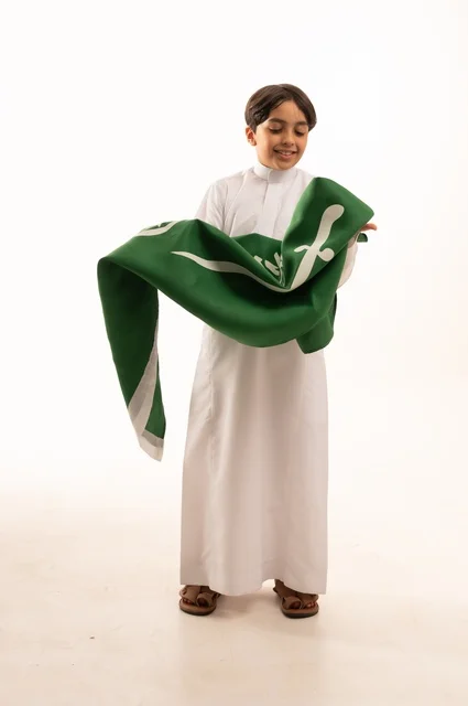 إيماءات السعادة والسرور، ذكرى اليوم الوطني السعودي 23سبتمبر، الفخر والاعتزاز بامتلاك الهوية الوطنية، حب الوطن والانتماء إليه، بورتريه لولد عربي خليجي سعودي يرتدي الثوب التقليدي يحمل بيده علم المملكة ، الاحتفال بيوم العلم 11مارس، خلفية بيضاء