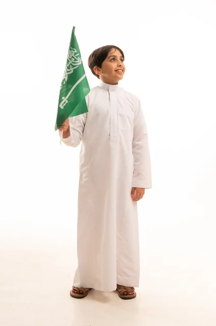 ذكرى اليوم الوطني السعودي 23سبتمبر، الفخر والاعتزاز بامتلاك الهوية الوطنية، حب الوطن والانتماء إليه، بورتريه لولد عربي خليجي سعودي يرتدي الثوب التقليدي يحمل بيده علم المملكة وينظر إلى شيء ما، الاحتفال بيوم العلم 11مارس، خلفية بيضاء