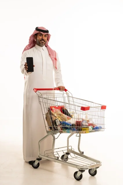 A blank black screen displayed on a mobile phone, enjoying shopping in shopping malls, buying essentials and necessities, taking advantage of discounts on products, a portrait of a Saudi Arabian Gulf man wearing traditional attire pushing a shopping cart with gestures of happiness, full-body, white background.