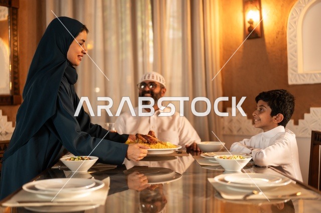 أداء فريضة الصيام في شهر رمضان المبارك، أجواء عائلية دينية رمضانية سعيدة، تبادل الأحاديث بين أفراد الأسرة، عائلة عربية خليجية سعودية مجتمعة حول مائدة الطعام، سفرة مليئة بأصناف من المأكولات الشرقية الشهية،  زينة المناسبات الإسلامية