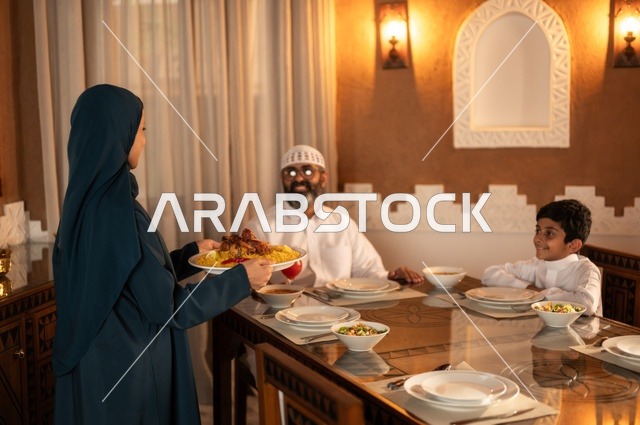 أجواء عائلية روحانية دينية إسلامية، ايماءات السرور لاجتماع العائلة حول مائدة إفطار رمضان، عائلة عربية خليجية سعودية مجتمعة حول مائدة الطعام، سفرة مليئة بأصناف من المأكولات الشرقية الشهية، أداء فريضة الصيام في شهر رمضان المبارك، موعد كسر الصيام عند الأذان
