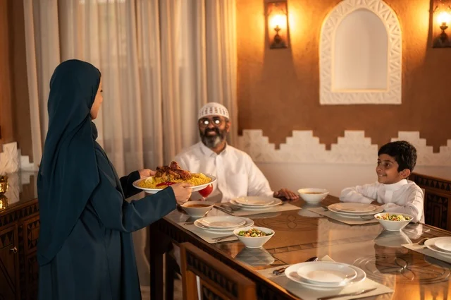 Spiritual and religious family atmosphere, gestures of joy for the family gathering around the Ramadan iftar table, an Arab Gulf Saudi family gathered around the dining table, a spread filled with a variety of delicious Eastern dishes, performing the fasting obligation in the blessed month of Ramadan, the time to break the fast at the call to prayer.
