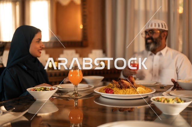 ايماءات السرور لاجتماع العائلة حول مائدة إفطار رمضان، أجواء عائلية روحانية دينية إسلامية، عائلة عربية خليجية سعودية مجتمعة حول مائدة الطعام، سفرة مليئة بأصناف من المأكولات الشرقية الشهية، أداء فريضة الصيام في شهر رمضان المبارك، موعد كسر الصيام عند الأذان