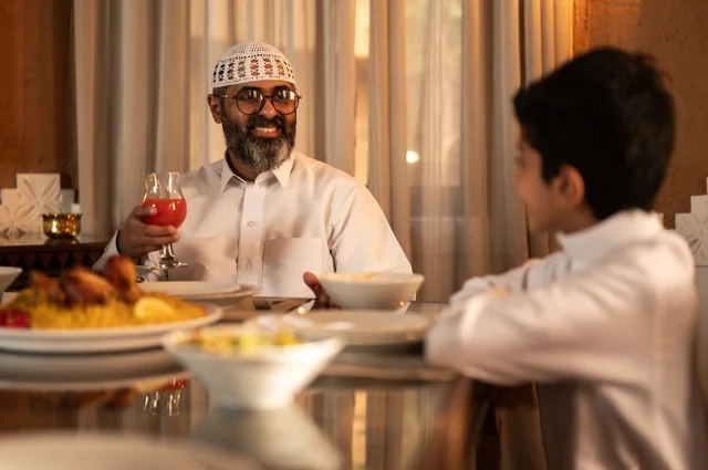 A table filled with a variety of delicious dishes, an Arab Gulf Saudi family at the iftar table during the month of Ramadan, a father and son enjoying their breakfast meal, joyful facial expressions, Ramadan atmosphere, Ramadan lantern, the holy month of Ramadan.