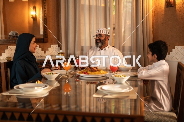 تبادل الأحاديث بين أفراد الأسرة، أجواء عائلية دينية رمضانية سعيدة، عائلة عربية خليجية سعودية مجتمعة حول مائدة الطعام، سفرة مليئة بأصناف من المأكولات الشرقية الشهية، أداء فريضة الصيام في شهر رمضان المبارك، زينة المناسبات الإسلامية