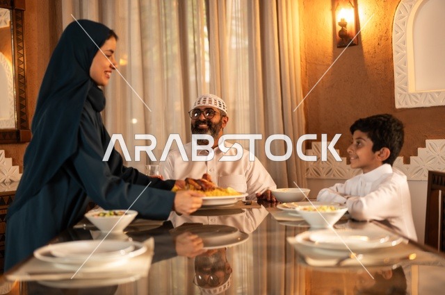 أداء فريضة الصيام في شهر رمضان المبارك، أجواء عائلية دينية رمضانية سعيدة، تبادل الأحاديث بين أفراد الأسرة، عائلة عربية خليجية سعودية مجتمعة حول مائدة الطعام، سفرة مليئة بأصناف من المأكولات الشرقية الشهية،  زينة المناسبات الإسلامية