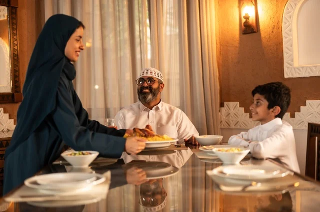 Performing the obligation of fasting in the blessed month of Ramadan, happy religious family Ramadan atmosphere, exchanging conversations among family members, an Arab Gulf Saudi family gathered around the dining table, a spread full of delicious Eastern dishes, decorations for Islamic occasions.
