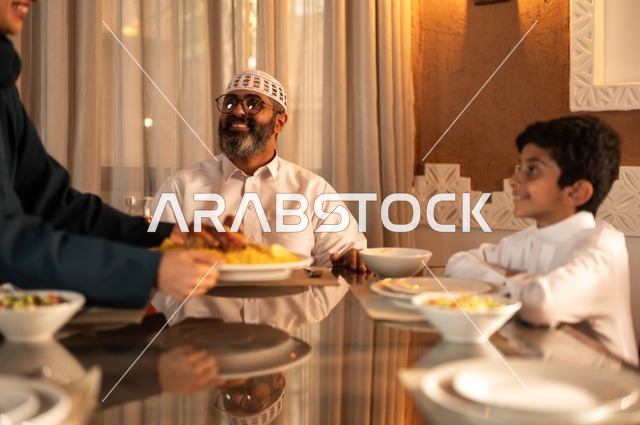 Expressions of joy for the family gathering around the Ramadan iftar table, a spiritual and religious Islamic family atmosphere, an Arab Gulf Saudi family gathered around the dining table, a spread filled with a variety of delicious Eastern dishes, performing the fasting obligation in the blessed month of Ramadan, the time to break the fast at the call to prayer.
