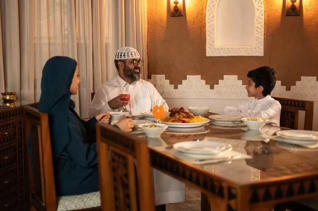 أجواء عائلية دينية رمضانية سعيدة، تبادل الأحاديث بين أفراد الأسرة، عائلة عربية خليجية سعودية مجتمعة حول مائدة الطعام، سفرة مليئة بأصناف من المأكولات الشرقية الشهية، أداء فريضة الصيام في شهر رمضان المبارك، زينة المناسبات الإسلامية