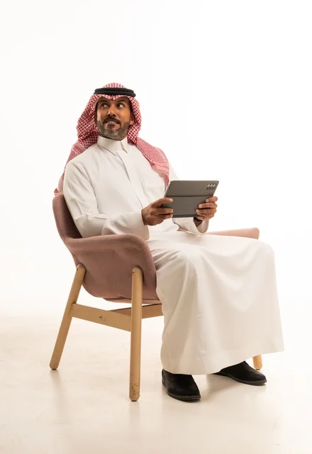الدردشة مع الأهل والأصدقاء، استعمال التكنولوجيا والتقنيات الحديثة، بورتريه لرجل عربي خليجي عماني يرتدي الثوب والشماغ التقليدي يحمل بيده جهاز التابلت، تصفح مواقع التواصل الاجتماعي، استخدام تطبيقات وبرامج الأجهزة اللوحية، خلفية بيضاء