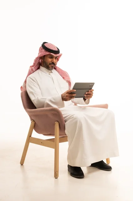 الدردشة مع الأهل والأصدقاء، استعمال التكنولوجيا والتقنيات الحديثة، بورتريه لرجل عربي خليجي عماني يرتدي الثوب والشماغ التقليدي يحمل بيده جهاز التابلت، تصفح مواقع التواصل الاجتماعي، استخدام تطبيقات وبرامج الأجهزة اللوحية، خلفية بيضاء