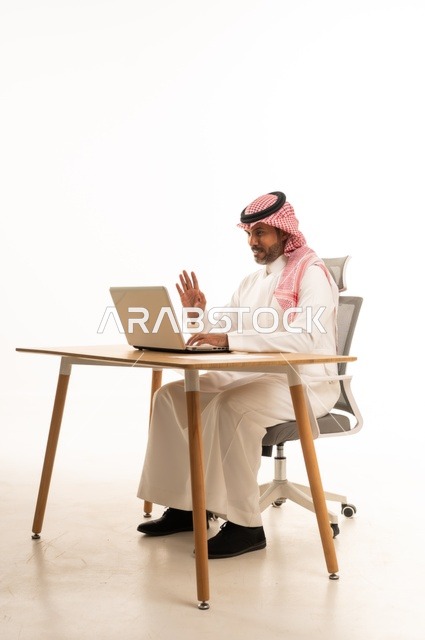 Communication with clients, completing work tasks online, using modern technology and techniques, a portrait of an Arab Gulf Omani man wearing traditional thobe and shmagh sitting behind holding a laptop, browsing social media, using mobile applications, white background.