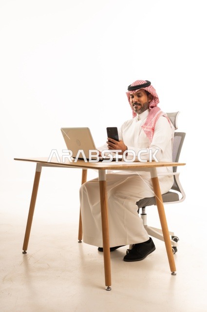 التواصل مع العملاء عبر الهاتف، انجاز مهام العمل عبر الانترنت، استعمال التكنولوجيا والتقنيات الحديثة، بورتريه لرجل عربي خليجي عماني يرتدي الزي التقليدي يجلس خلف يحمل بيده جهاز اللابتوب، تصفح مواقع التواصل الاجتماعي، استخدام تطبيقات الأجهزة المحمولة، خلفية بيضاء