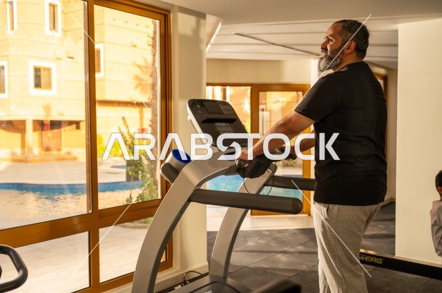 استخدام الاجهزة الرياضية، ممارسة تمارين الاحماء, المحافظة على الصحة واللياقة البدنية, شاب عربي خليجي سعودي يرتدي الملابس الرياضية يقوم بالمشي على الجهاز الكهربائي، نادي الألعاب الرياضية, القيام بالأنشطة الترفيهية الممتعة