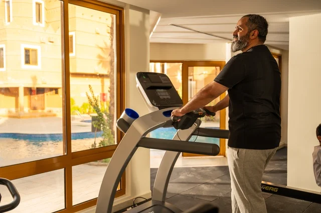 Using sports equipment, practicing warm-up exercises, maintaining health and physical fitness, a young Arab Gulf Saudi man wearing sports clothes walking on the treadmill, sports club, engaging in enjoyable recreational activities.