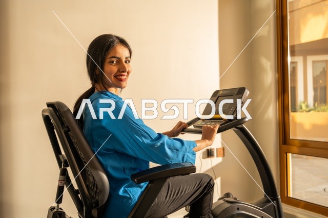 Physical activities to maintain fitness and agility, gestures of happiness and activity, following a healthy lifestyle using technological devices, sports to strengthen muscles and sculpt the body, a side image of a young Arab Gulf Saudi woman wearing sportswear exercising.