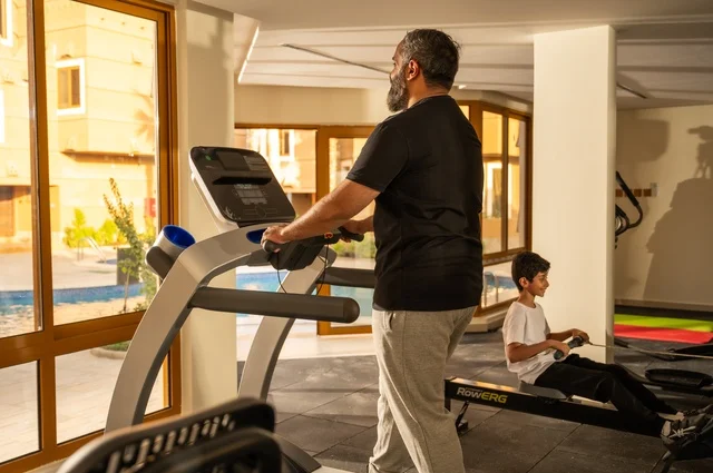 Warming up exercises, maintaining health and physical fitness, a young Arab Gulf Saudi man wearing sportswear walking on the treadmill, sports club, engaging in enjoyable recreational activities, using fitness equipment.