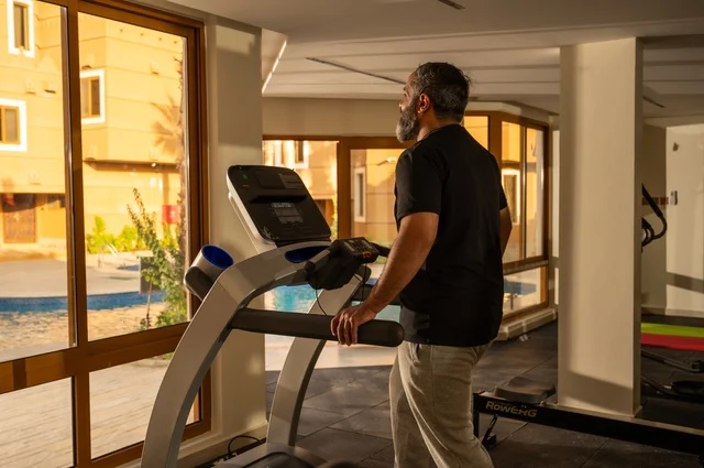Maintaining health and fitness, practicing warm-up exercises, a young Arab Gulf Saudi man wearing sportswear walking on the treadmill, sports club, engaging in enjoyable recreational activities, using fitness equipment.