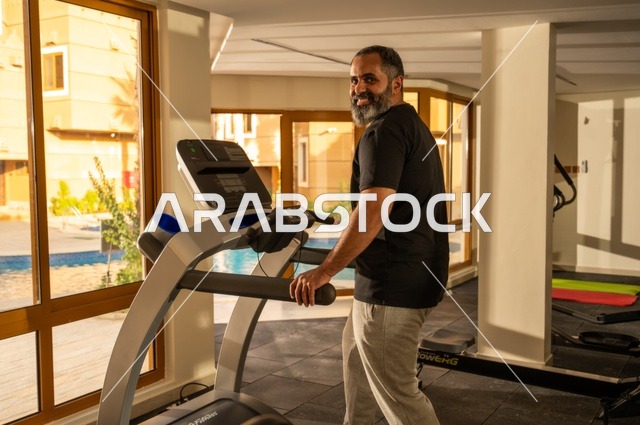 Maintaining health and fitness, practicing warm-up exercises, a young Arab Gulf Saudi man wearing sportswear walking on the treadmill, sports club, engaging in enjoyable recreational activities, using fitness equipment.