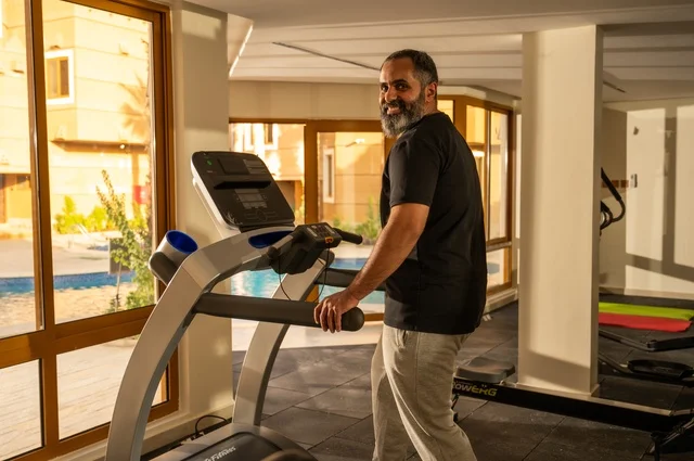 Maintaining health and fitness, practicing warm-up exercises, a young Arab Gulf Saudi man wearing sportswear walking on the treadmill, sports club, engaging in enjoyable recreational activities, using fitness equipment.