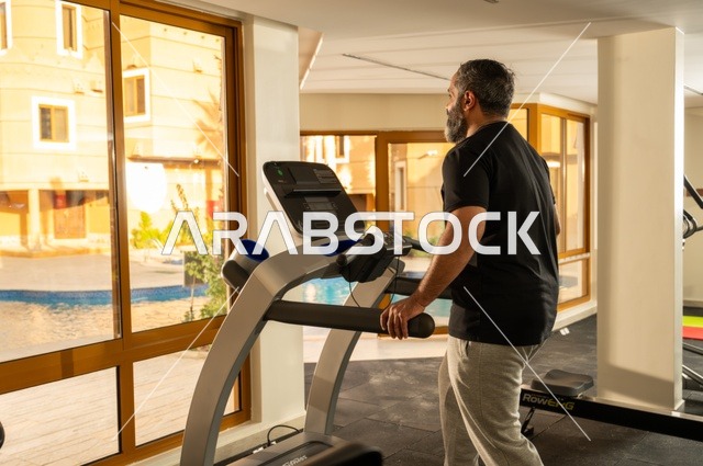 استخدام الاجهزة الرياضية، ممارسة تمارين الاحماء, المحافظة على الصحة واللياقة البدنية, شاب عربي خليجي سعودي يرتدي الملابس الرياضية يقوم بالمشي على الجهاز الكهربائي، نادي الألعاب الرياضية, القيام بالأنشطة الترفيهية الممتعة